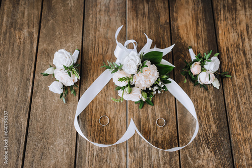 A bouquet of flowers with a ribbon in the form of a heart, a boutonniere, golden rings of the newlyweds lie on a wooden background. Wedding photography, top view.