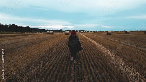 Girl walking through a field with bales of hay in the evening