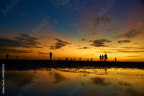 Silhouettes of people walking on the ocean floor after the evening tide. Incredible colors of the evening sky © Kate
