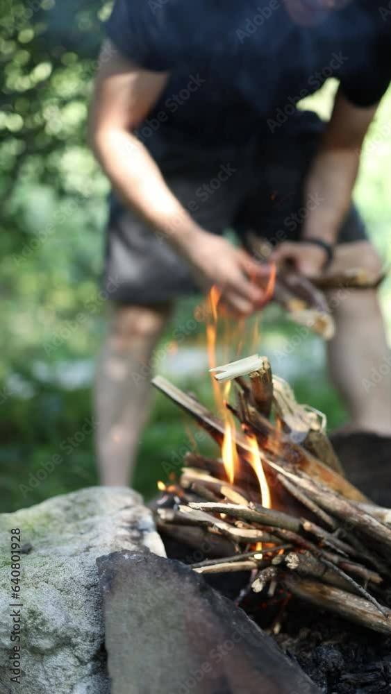 male hands put wood on the fire in the forest in nature. vertical video. lighting a bonfire male hands put wood on the fire in the forest in nature. vertical video. lighting a bonfire