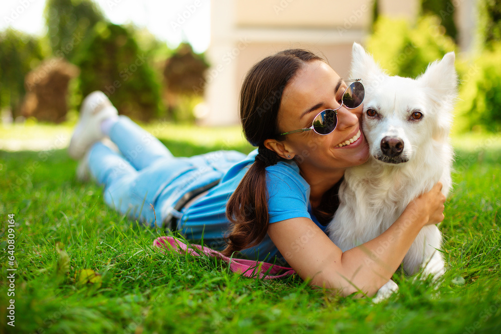 Happy young pretty brunette girl hugging her cute white fluffy dog on the outdoor in the park on lawn. Adoption, rescued, shelter, companion, pet. Happy young pretty brunette girl hugging her cute white fluffy dog on the outdoor in the park on lawn. Adoption, rescued, shelter, companion, pet.