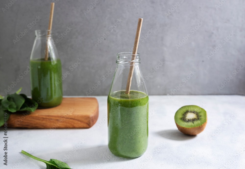 Green smoothie from banana, apple, spinach and kiwi in glass bottles on a light gray background. Healthy green smoothie. Green smoothie from banana, apple, spinach and kiwi in glass bottles on a light gray background. Healthy green smoothie.