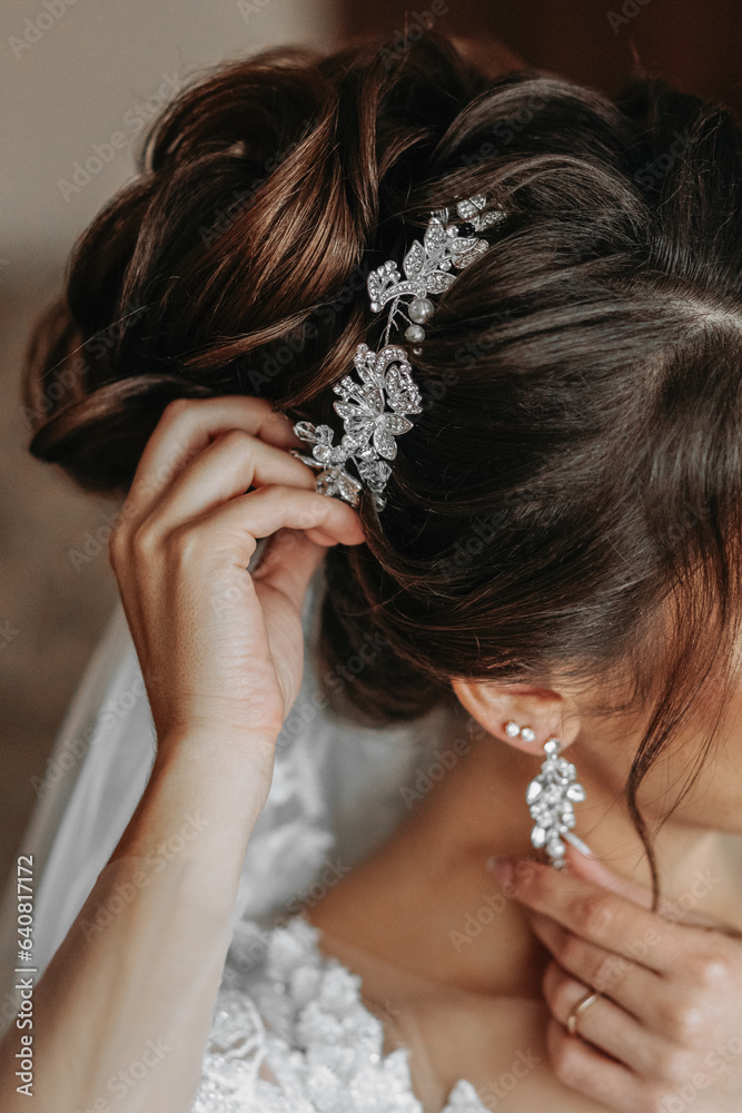 The hairdresser makes a fashionable and stylish styling on the bride's hair. Beautifies a hairdress with a beautiful precious accessory made of white beads