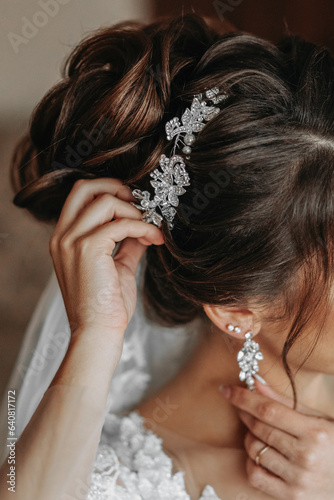 The hairdresser makes a fashionable and stylish styling on the bride's hair. Beautifies a hairdress with a beautiful precious accessory made of white beads