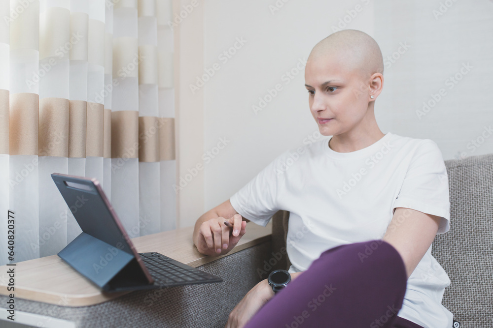 Naklejka premium Young bald woman with oncology after chemotherapy is studying remotely at home.