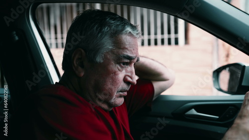 Elderly man suffering emotional pain inside car, parked in street. Dramatic lonely older person in desperate dire circumstances, struggling in quiet despair, socially disconnected