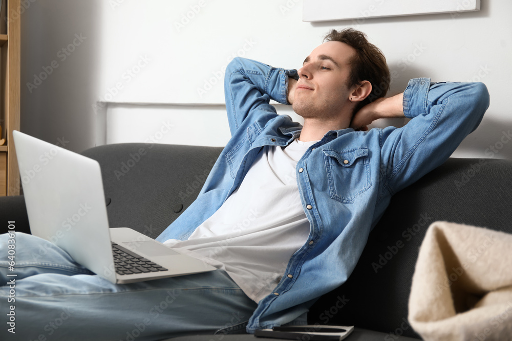 Male freelancer with laptop resting on sofa at home