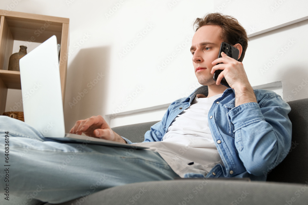 Male freelancer with laptop talking by mobile phone on sofa at home Male freelancer with laptop talking by mobile phone on sofa at home