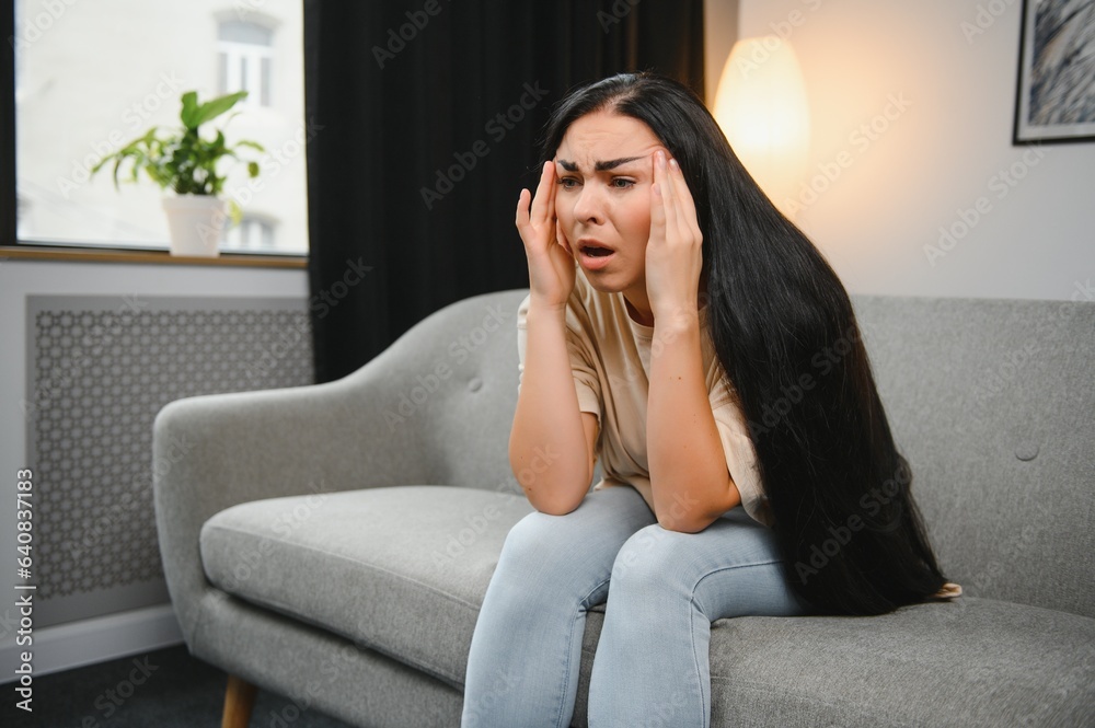 girl holding her head, woman has a headache. sad female sitting on couch