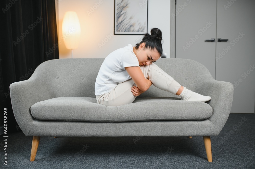 Portrait of beautiful young woman with depressed facial expression sitting on grey textile couch. Cyber bullying victim concept. Sad female in her room. Background, copy space