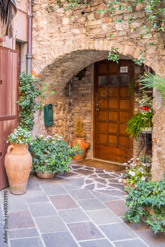 Historic house entrance in a small Italian town, hidden in a brick archway. The entrance is decorated with planters and green plants and invites you into a pleasantly cool apartment.