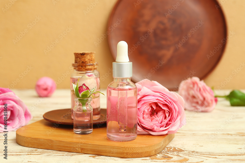 Bottles of cosmetic oil with rose extract and flowers on light wooden table Bottles of cosmetic oil with rose extract and flowers on light wooden table