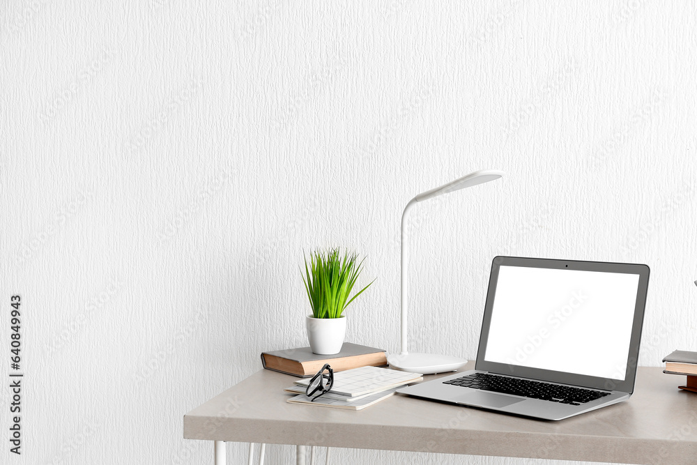 Comfortable workplace with modern laptop, books and houseplant on beige table Comfortable workplace with modern laptop, books and houseplant on beige table