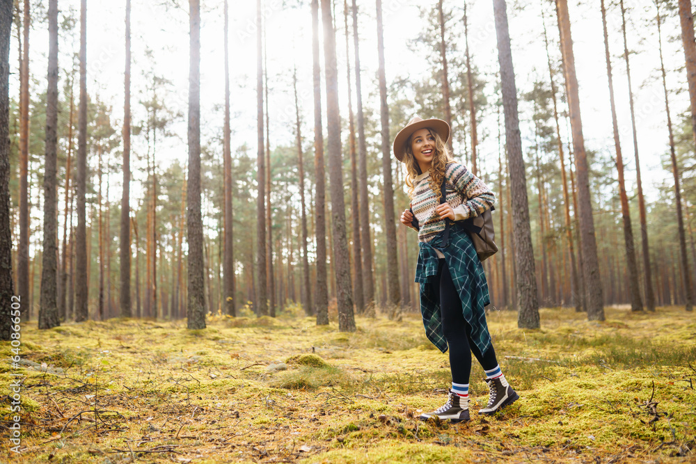 Active young woman with a backpack and a hat enjoys a beautiful autumn day in the forest, exploring the thicket of the forest. Traveler is walking along a footpath in the forest. Active young woman with a backpack and a hat enjoys a beautiful autumn day in the forest, exploring the thicket of the forest. Traveler is walking along a footpath in the forest.