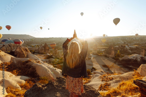 Canvas Print Woman tourist in a hat stands with her back on a mountain, looking at the balloons in Cappadocia, Turkey