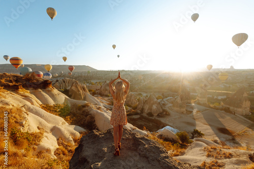 Canvas Print Woman tourist in a hat stands with her back on a mountain, looking at the balloons in Cappadocia, Turkey
