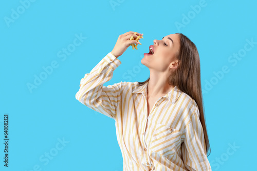 Beautiful young woman eating french fries on blue background