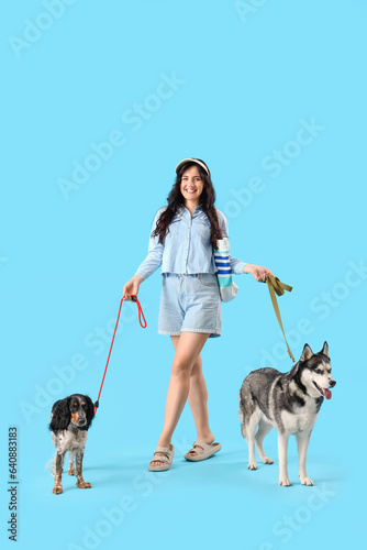 Young woman with cute dogs walking on blue background