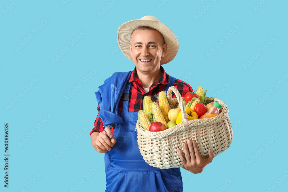 Mature male farmer with wicker basket full of different ripe vegetables on blue background Mature male farmer with wicker basket full of different ripe vegetables on blue background