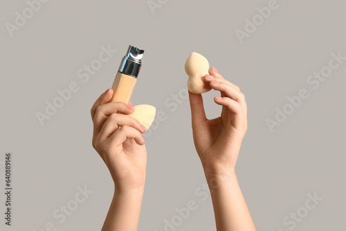 Female hands with makeup sponges and bottle of foundation on grey background
