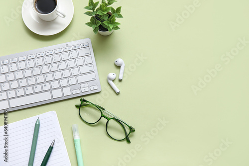 Keyboard, cup of coffee and stationery on light green background