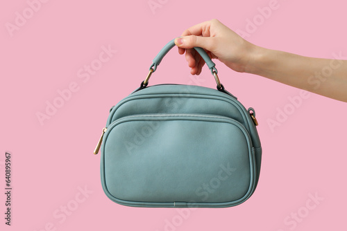 Female hand with stylish blue handbag on pink background