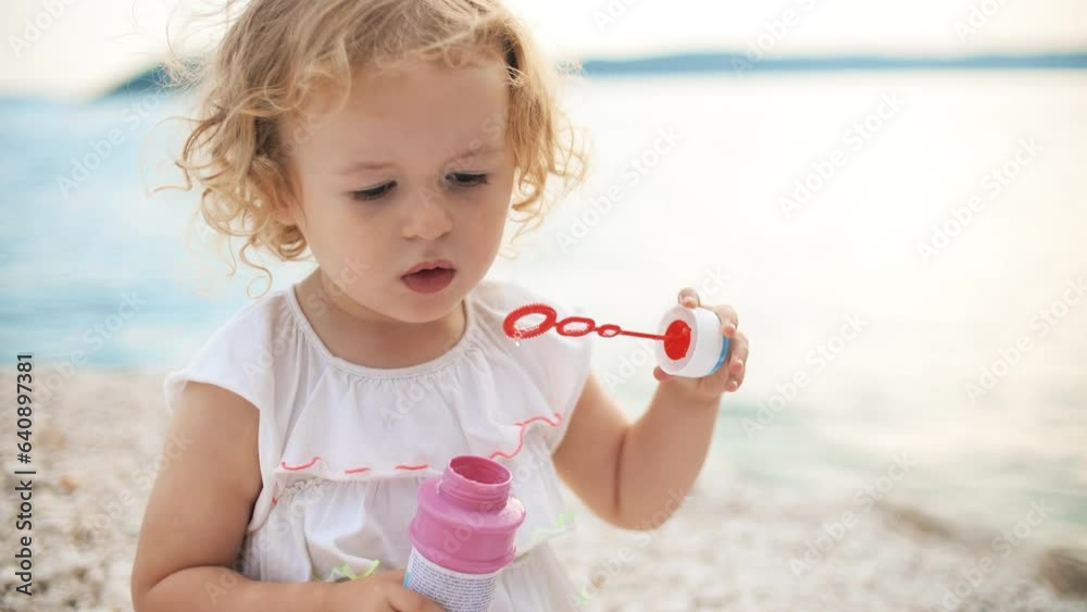 Curly little girl makes soap bubbles on the beach Curly little girl makes soap bubbles on the beach