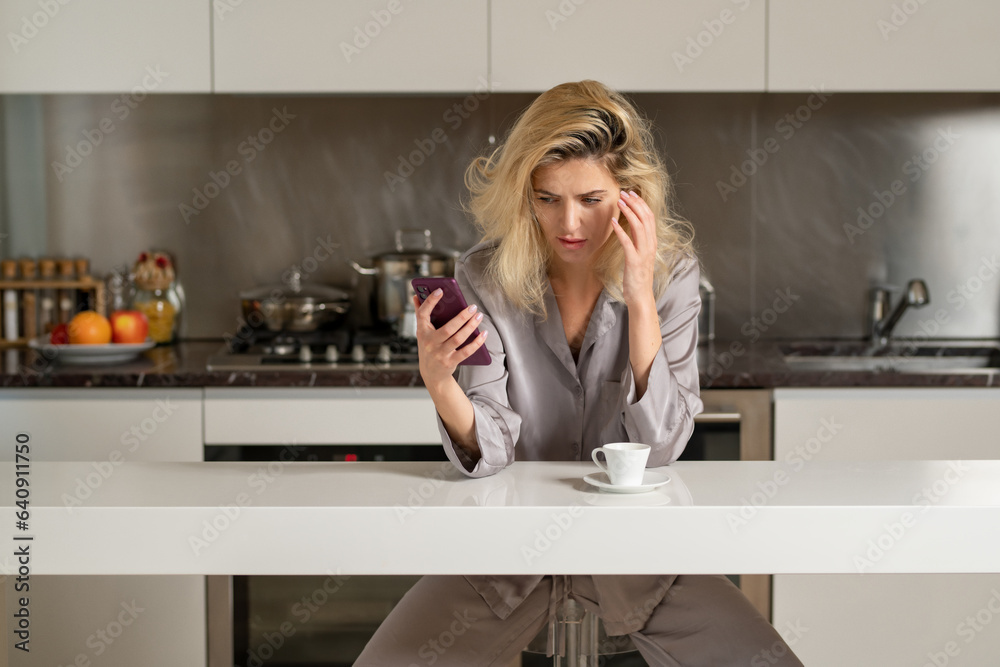 Annoyed housewife drink coffe at kitchen. Depressed woman in the kitchen in the morning. Sad woman chatting on phone in the kitchen in the morning.