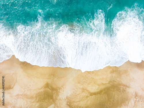 Aerial overhead photograph of a beach. Golden sand and turquoise water. The ocean water merges with the sand of the beach. 