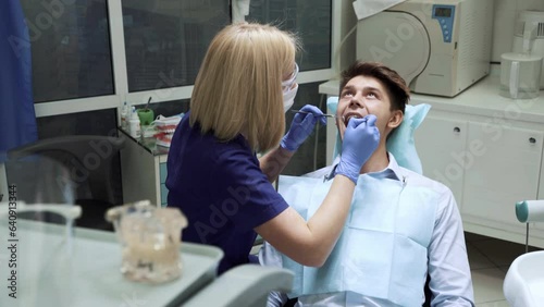 Portrait of young woman dentist sitting back examining teeth of male patient using mirror modern dentistry equipment in clinic hospital cabinet. Stomatoligy medical health care concept. Oral hygiene photo