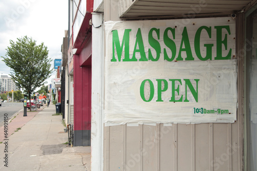 massage open 1030am to 9pm sign in green capital letters on white background screen right on store inner wall with sidewalk and road with distance screen left photo