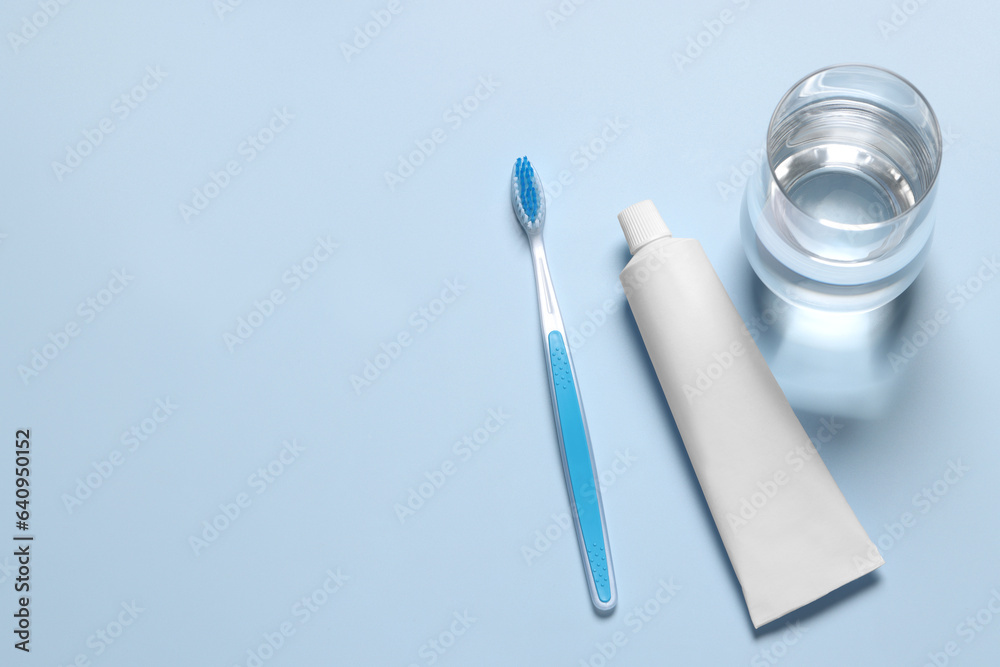 Plastic toothbrush with paste and glass of water on light background, above view. Space for text Plastic toothbrush with paste and glass of water on light background, above view. Space for text