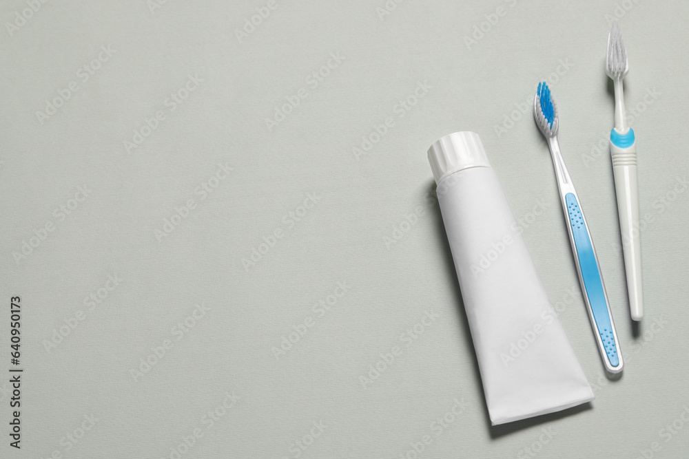 Plastic toothbrushes and paste on grey background, flat lay. Space for text Plastic toothbrushes and paste on grey background, flat lay. Space for text