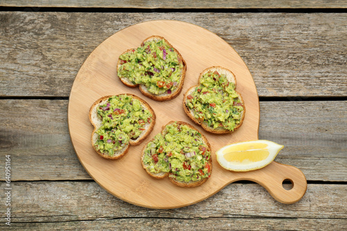 Slices of bread with tasty guacamole and lemon on wooden table, top view