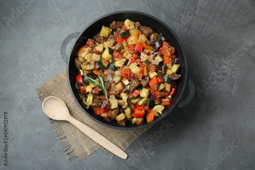Delicious ratatouille in baking dish and wooden spoon on grey table, flat lay