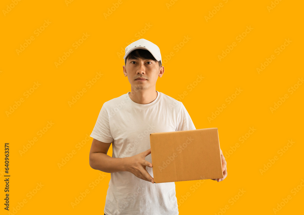 Young Asian delivery man wearing cap and white blank t-shirt holding parcel post box isolated on yellow background. express delivery service concept. Young Asian delivery man wearing cap and white blank t-shirt holding parcel post box isolated on yellow background. express delivery service concept.
