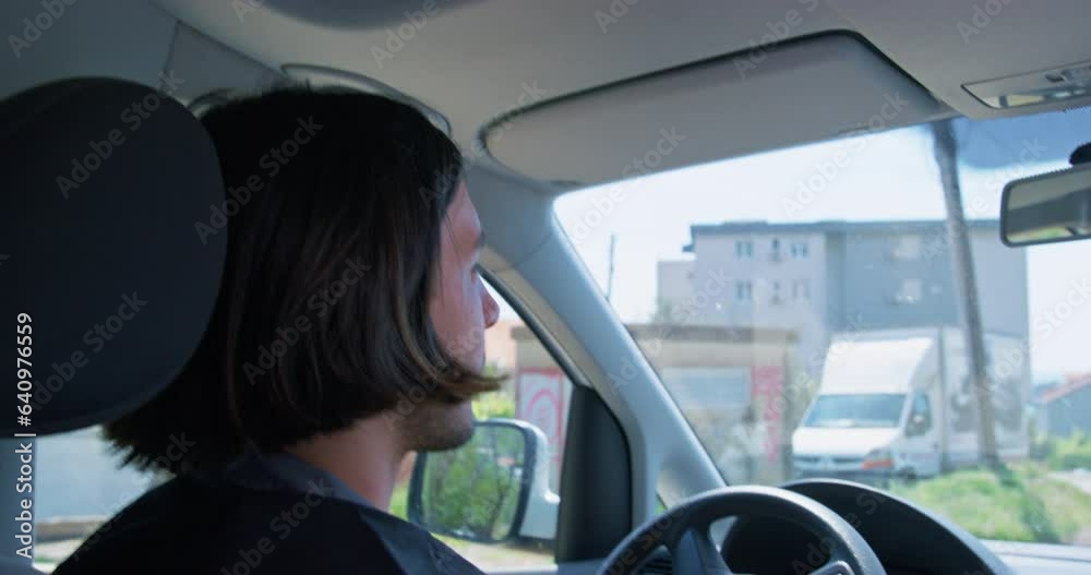 Long-haired man drives car on city street looking to side and getting scared. Worried driver turns steering wheel trying to escape follower closeup