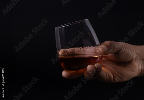 Hand holding glass of whiskey on black background
