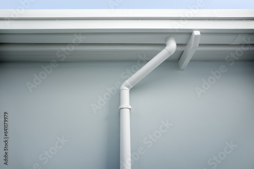 Rain gutter install on steel structure, connect to pvc downpipe or downspout, elbow at eaves, exterior house building. Also called guttering or eavestrough for water drainage system. Look new clean.