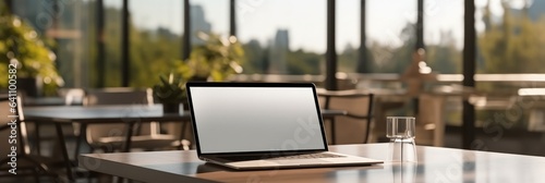 Laptop with blank white desktop screen on a modern meeting table in a contemporary room.