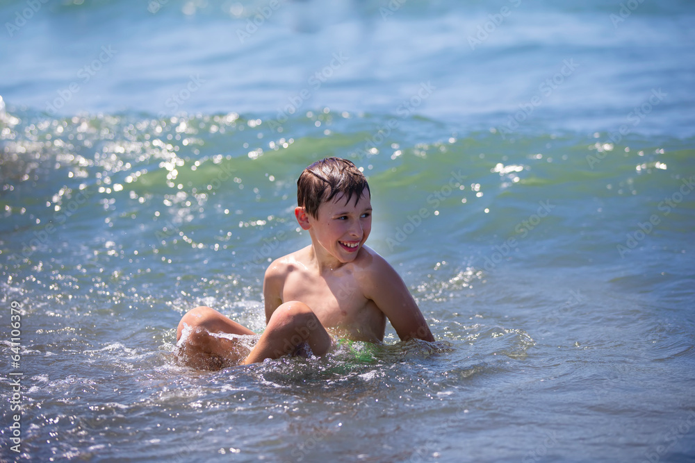 Happy boy swims in the sea, plays with the waves. Child on vacation at the seaside.