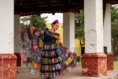 Mexican folk dancer woman from the state of nayarit, Mexican pink nayarrita folk costume with blue, fan and dancing with skirt and turns on black background photo