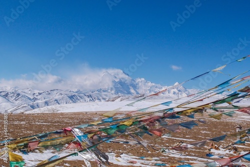 Mt. Shishapangma, its peak engulfed in a snowstorm, with Tibetan prayer flags fluttering in the foreground. Captured from the Tong La pass at 5,130 meters in Tibet. photo
