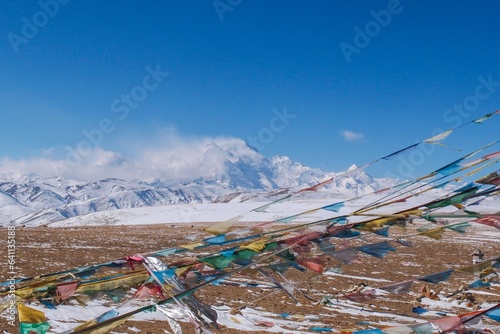 Mt. Shishapangma, its peak engulfed in a snowstorm, with Tibetan prayer flags fluttering in the foreground. Captured from the Tong La pass at 5,130 meters in Tibet.