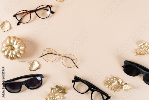 Eyewear and sunglasses sale concept. Trendy sunglasses on a beige background with a pumpkin and golden leaves. Trendy Fashion fall accessories. Copy space for text. Autumn sale. Optic store discount