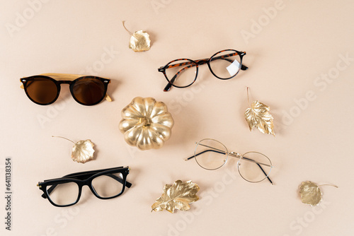 Trendy sunglasses of different design and eyeglasses on beige background with golden leaves. Close up. Sunglass and spectacles sale concept. Optics shop fall promotion poster. Autumn Eyewear fashion