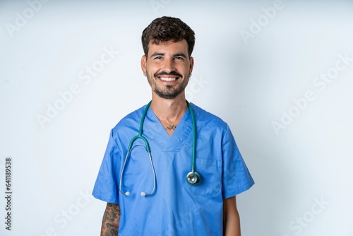 Canvas Print young caucasian doctor man wearing blue medical uniform with nice beaming smile pleased expression