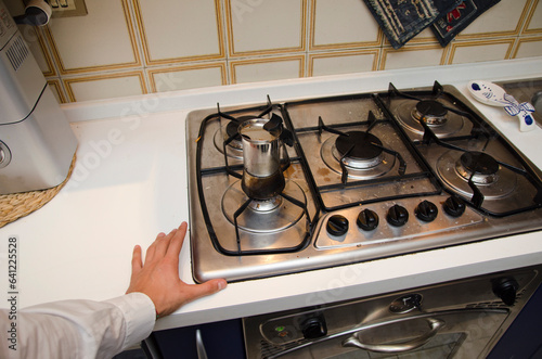 Obraz na plátně Photo of a person reaching for a pot on a stove