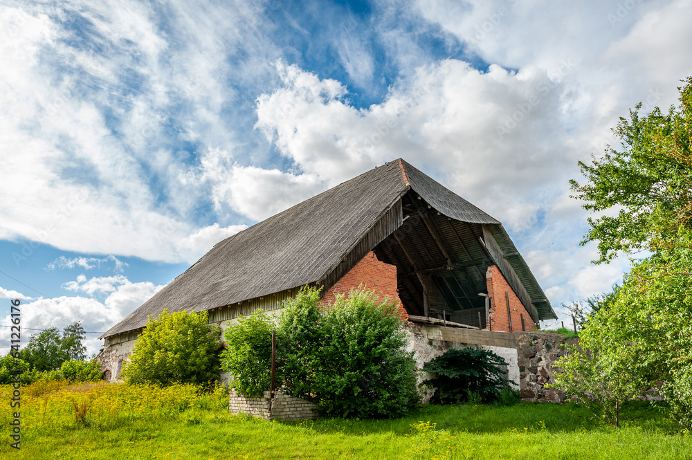 Fototapeta premium View of abandoned barn and dynamic sky. Weathered and worn red barn on an abandoned farm. Latvia.