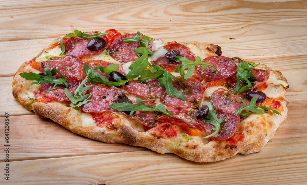 Pizza Diavolo with chorizo, rucola, jalapeno, chili, kalamata, pesto. Roman pizza rectangular on wood background